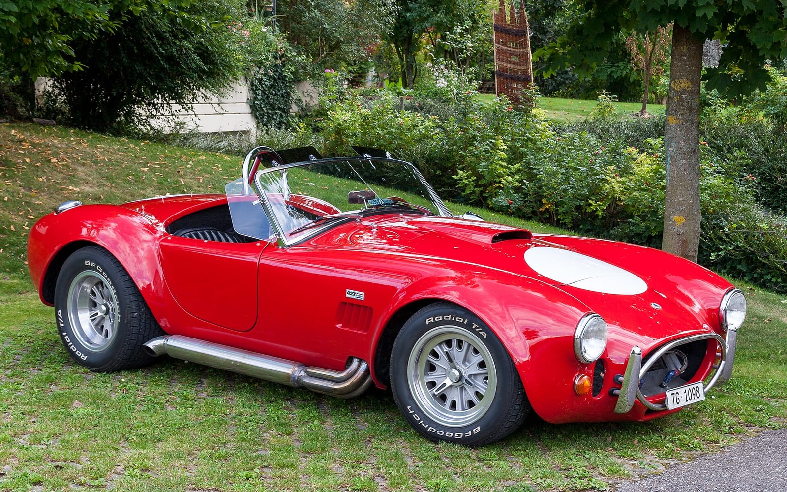 Red AC Cobra 427 roadster parked on grass