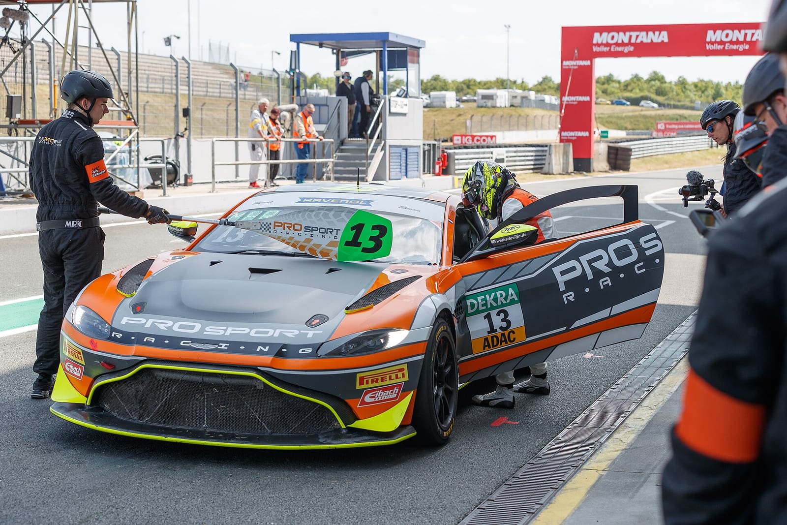 A driver climbing out of an Aston Martin GT4 car in the pit lane while a mechanic waits