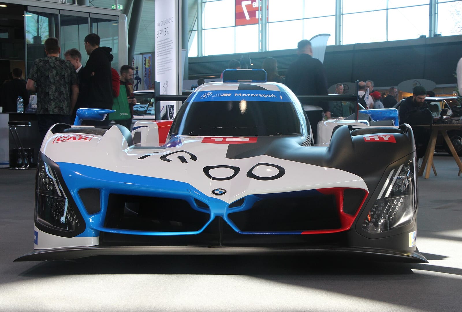 Front view of a BMW M Hybrid V8 prototype in white, blue and red BMW M Motorsport colours on display at a show