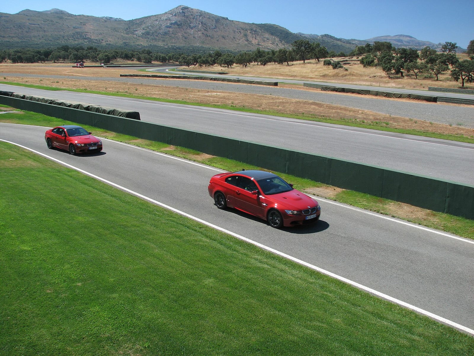 Two red BMW M3 E92 coupes driving on a race track