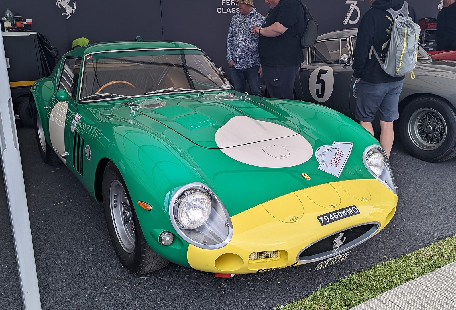 A green and yellow Ferrari 250 GTO parked in a paddock