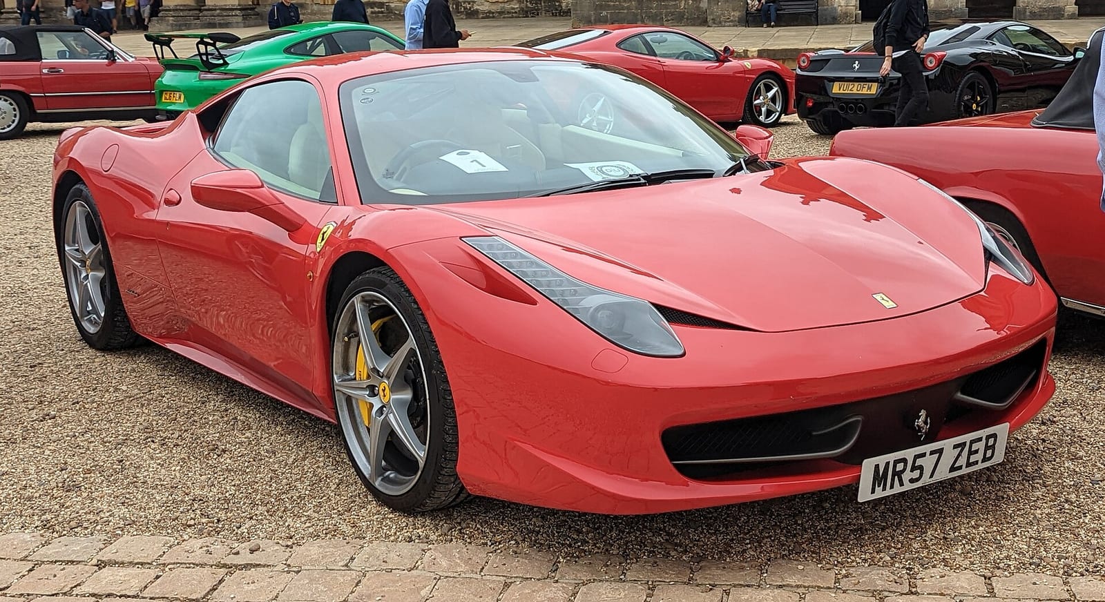 A red Ferrari 458 Italia parked on gravel at a car meeting