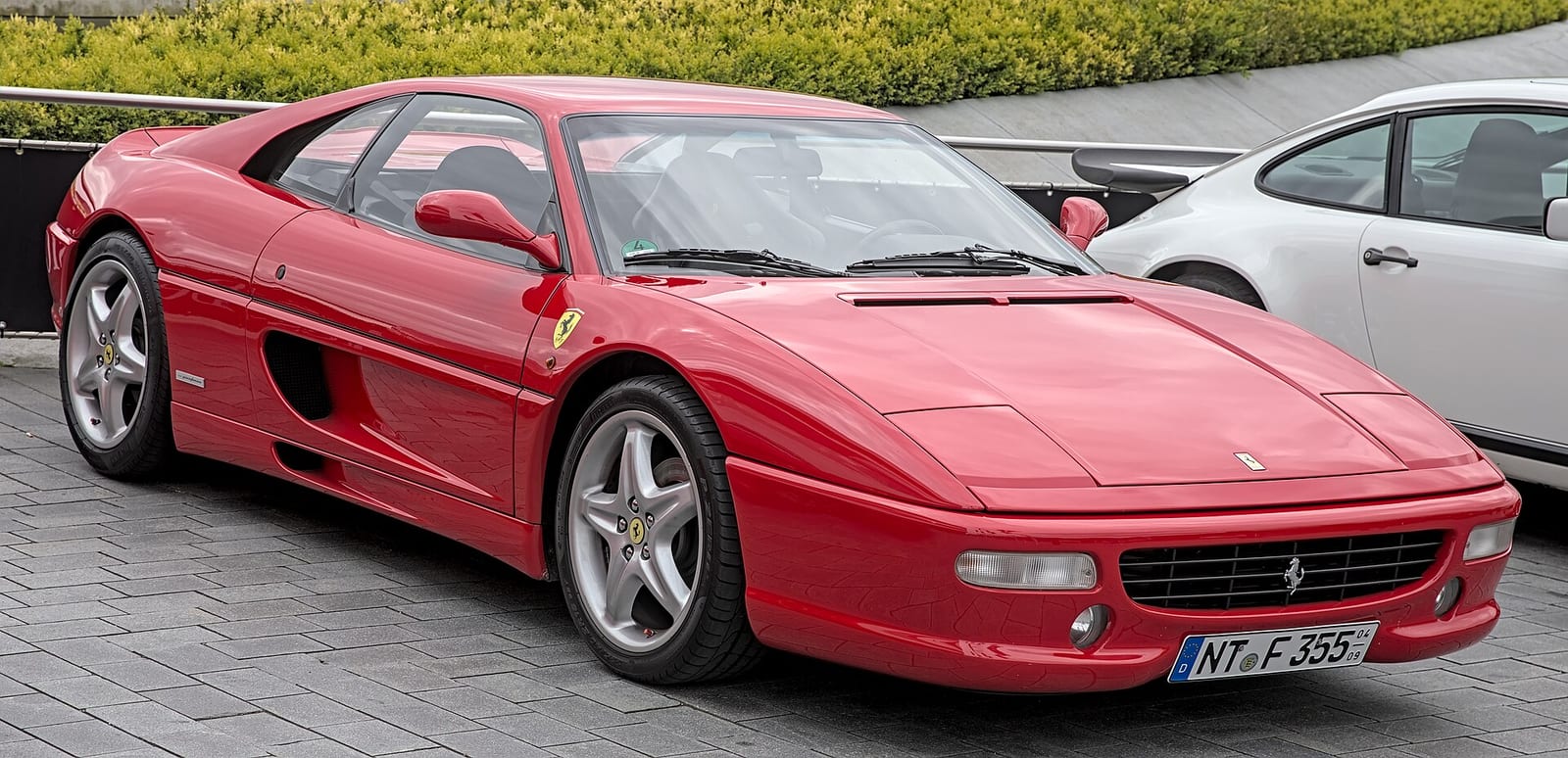 Red Ferrari F355 Berlinetta parked on a paved square, front three quarter view
