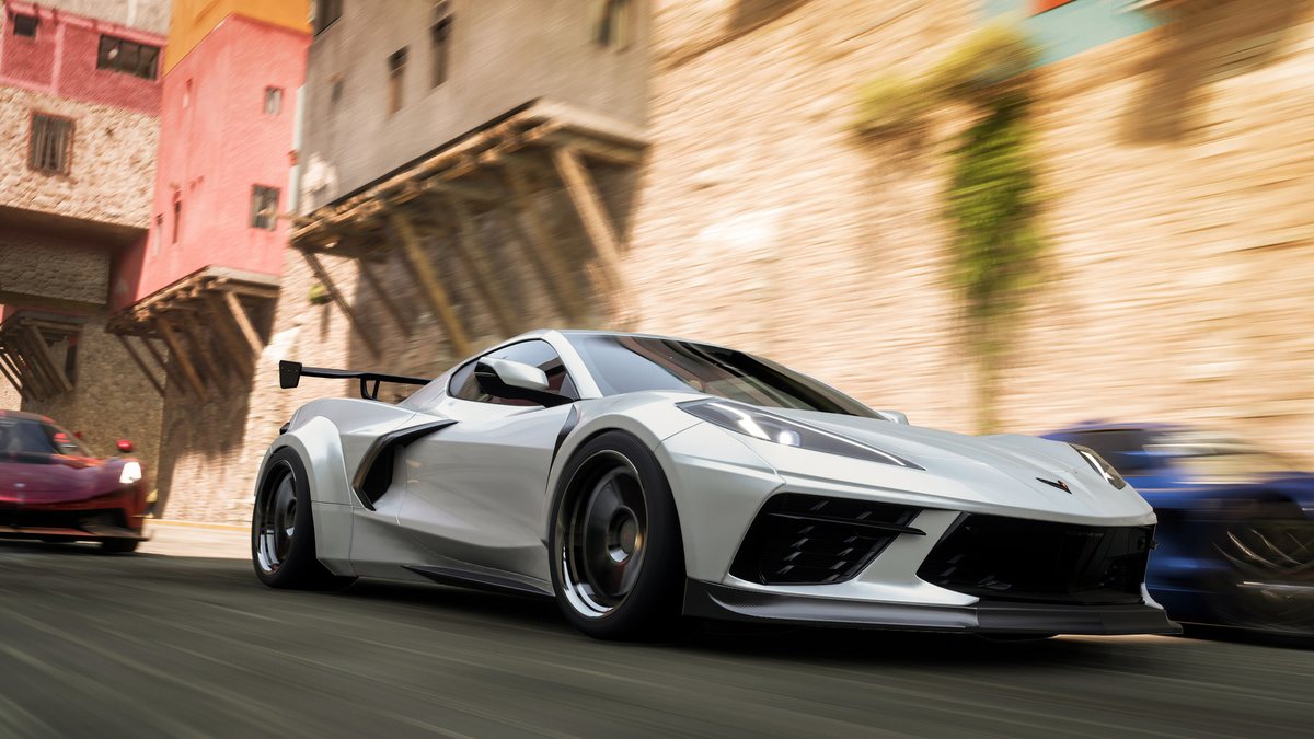 A white sports car races through a town street with other cars behind it in Forza Horizon 5