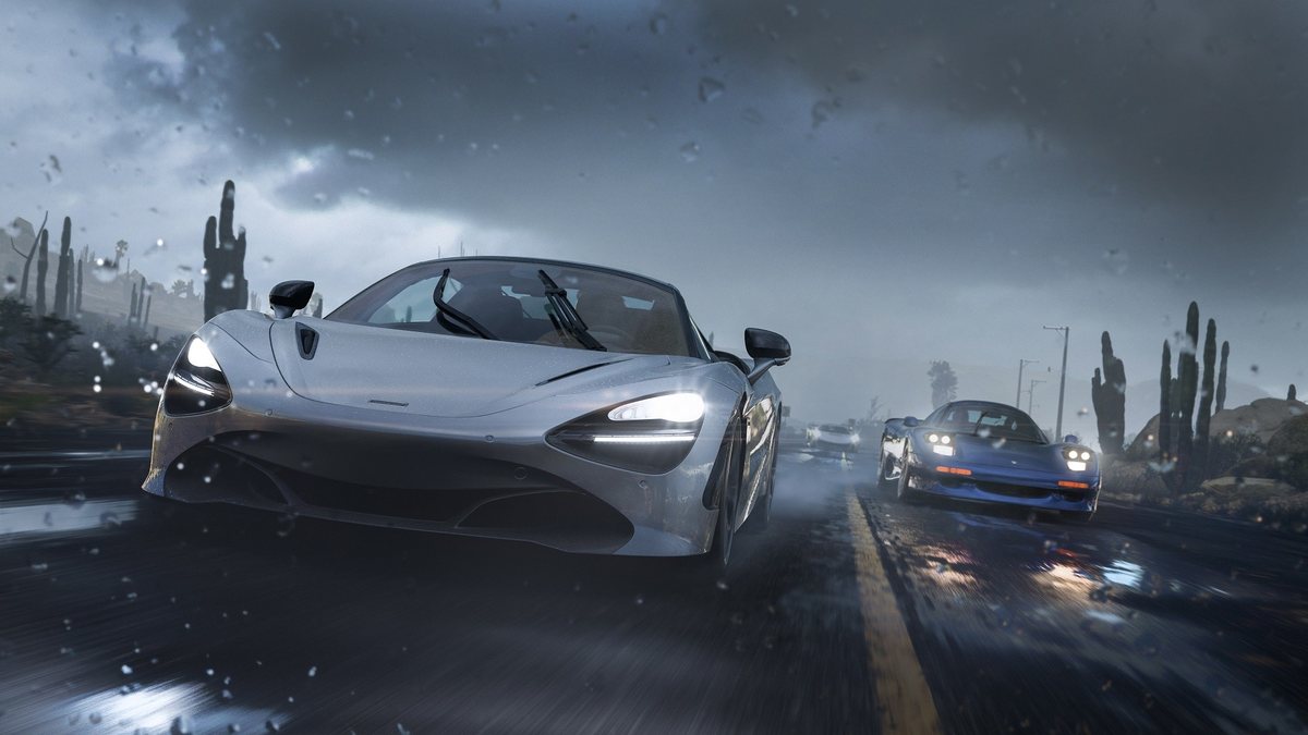 A grey supercar with its lights on drives a wet desert road under a dark sky in Forza Horizon 5