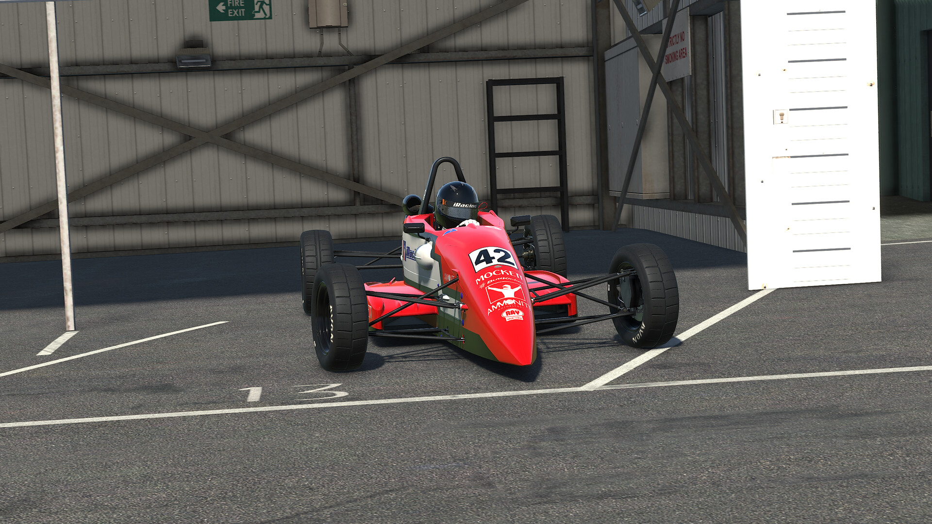 An open-wheel car parked in the iRacing garage with the pit wall boards beside it