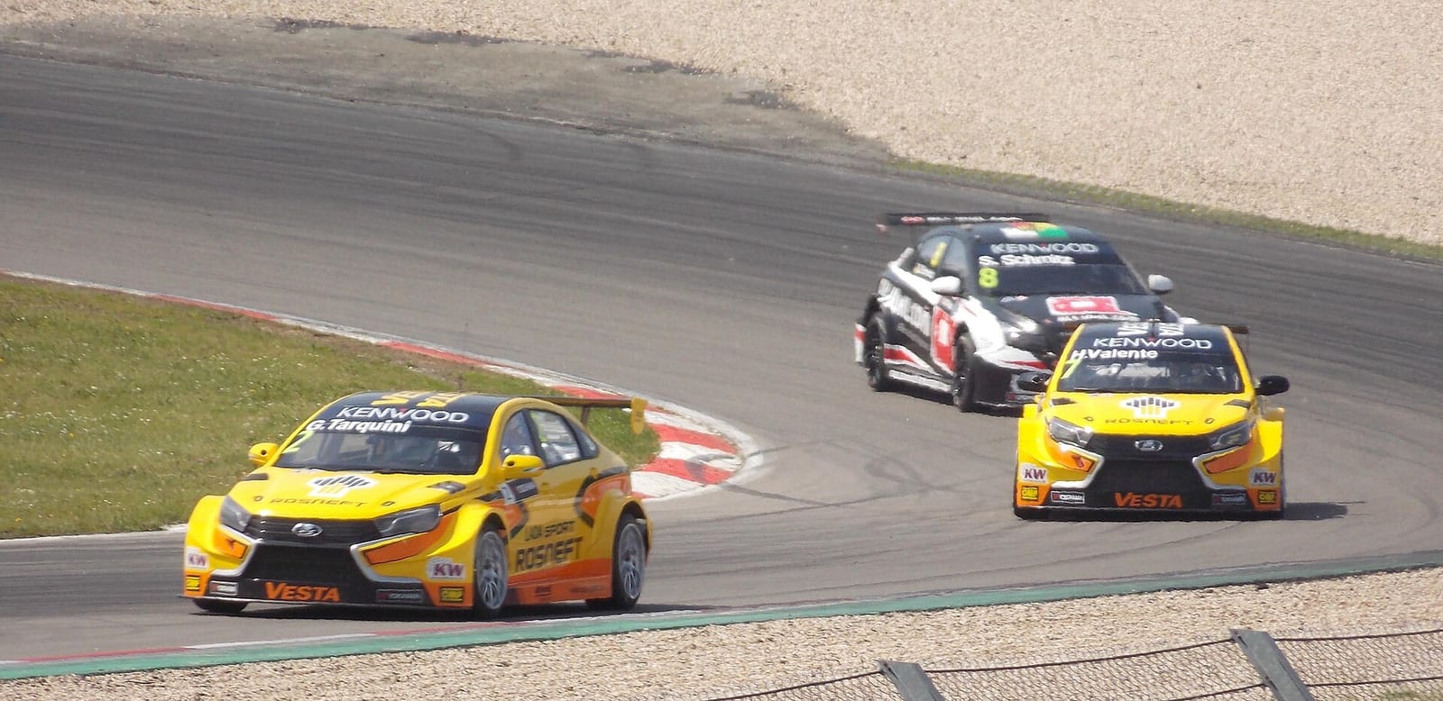 Two yellow Lada Vesta touring cars leading another car through a corner at the Nurburgring