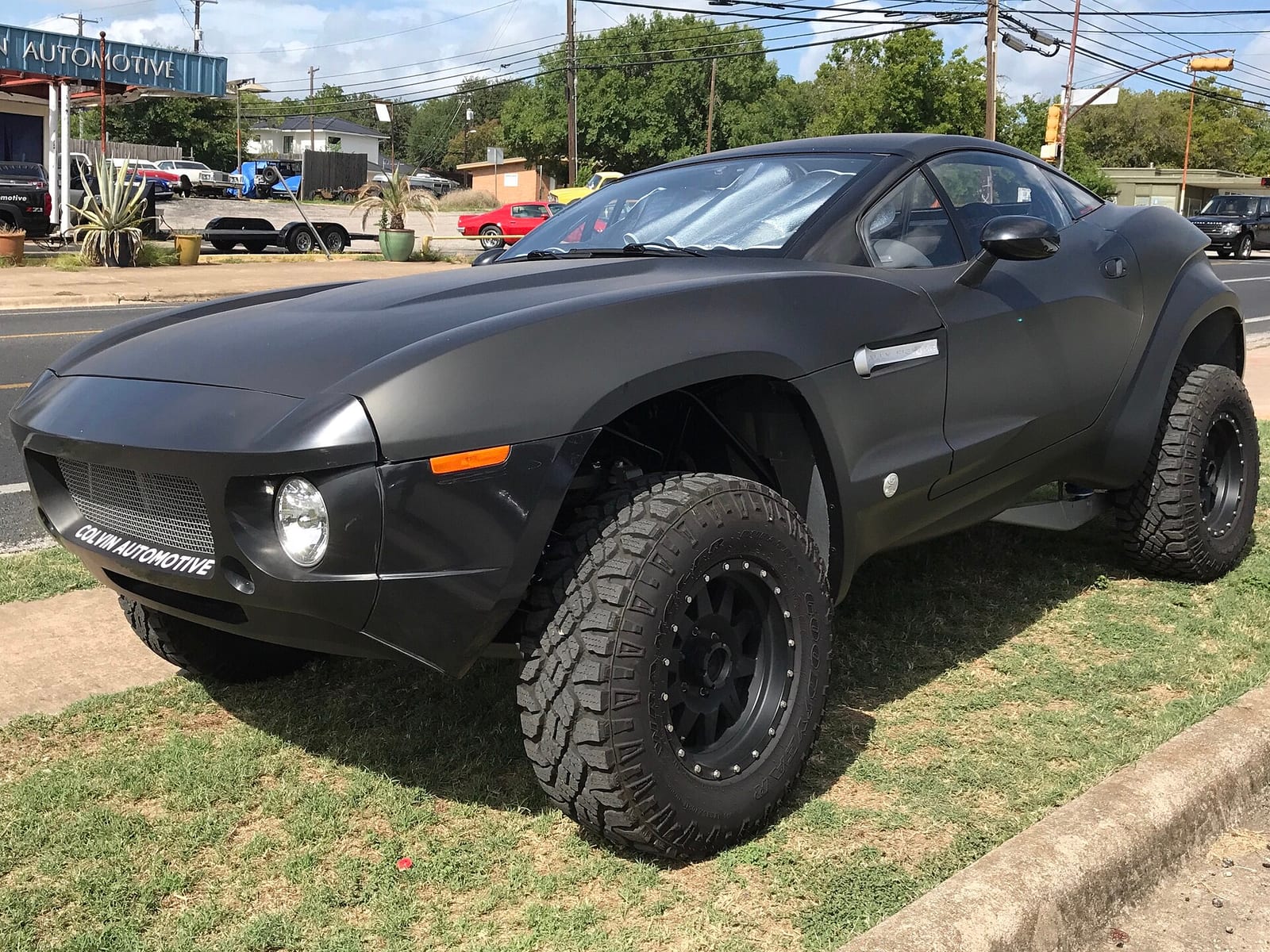 A matt black Local Motors Rally Fighter with tall off-road tyres parked on grass