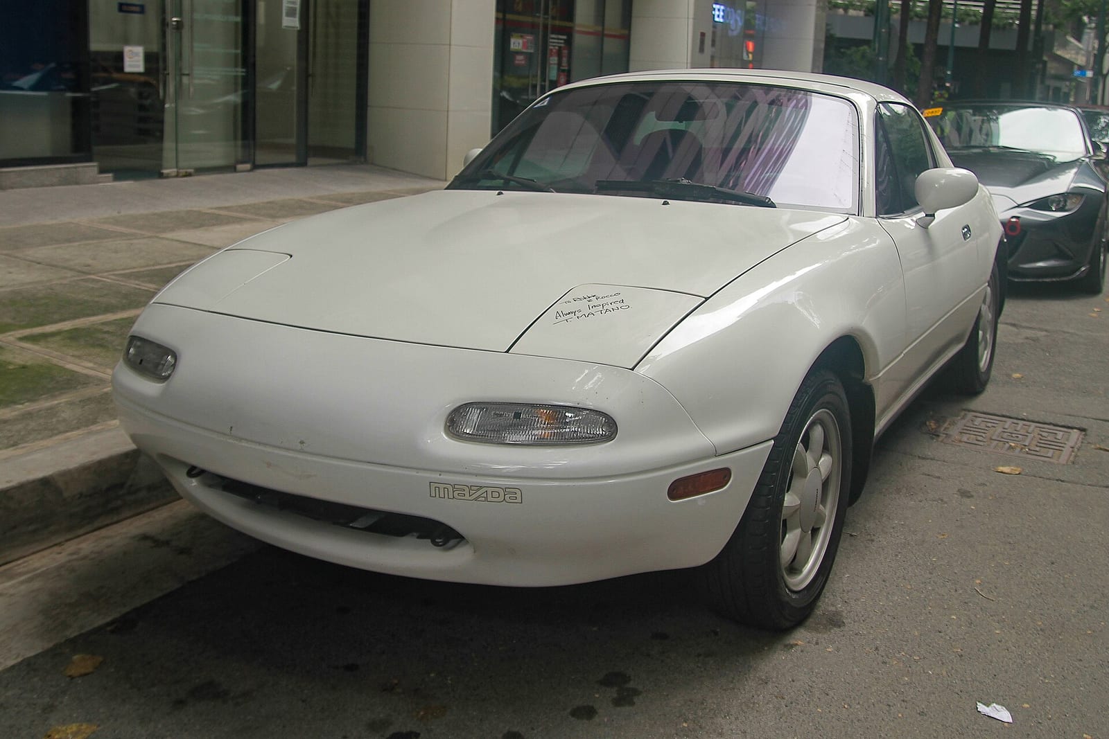 A white first generation Mazda MX-5 Miata with a hardtop