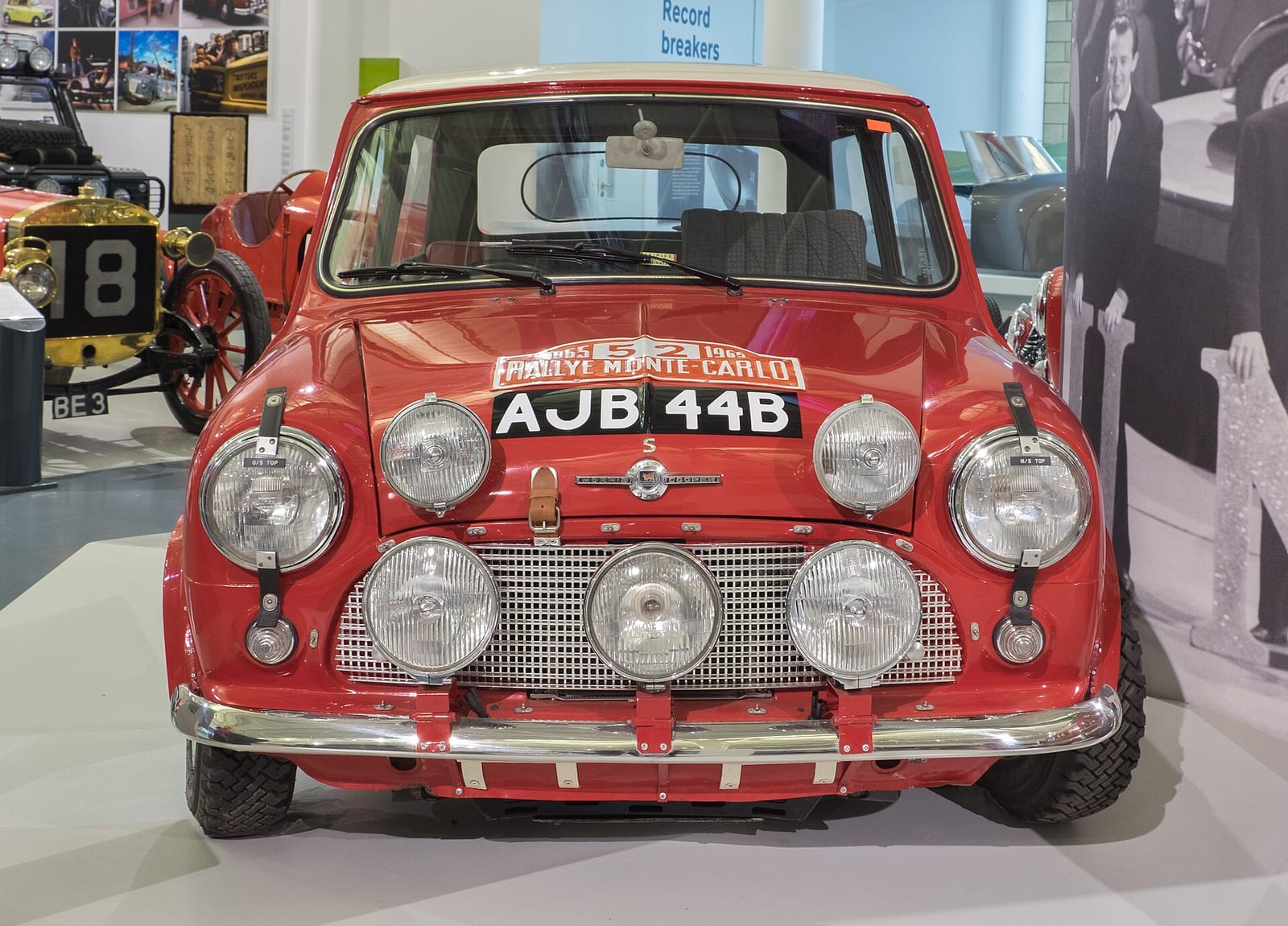 A red 1964 Mini Cooper S with rally lamps on the front, in a museum