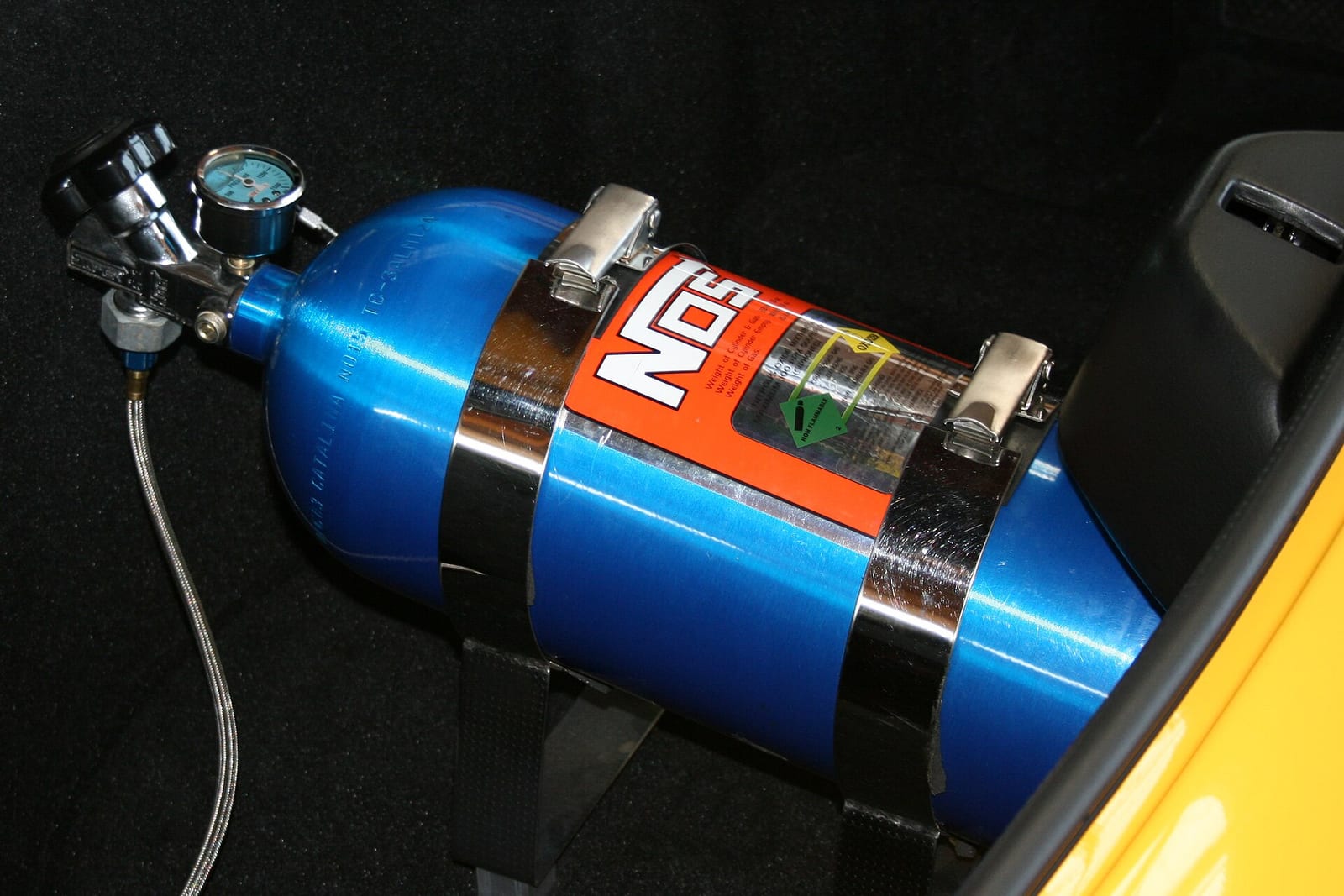 A blue nitrous oxide bottle strapped into the boot of a car, with a pressure gauge and a braided line