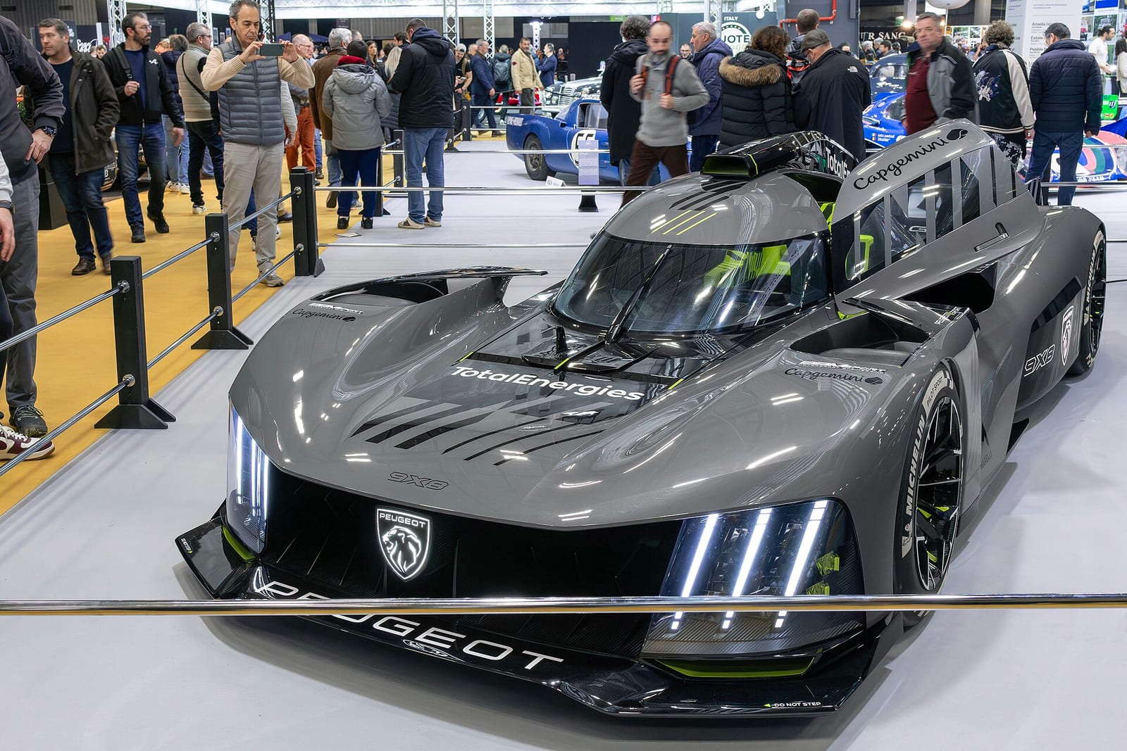 A grey Peugeot 9X8 hypercar on display at a show with visitors behind it