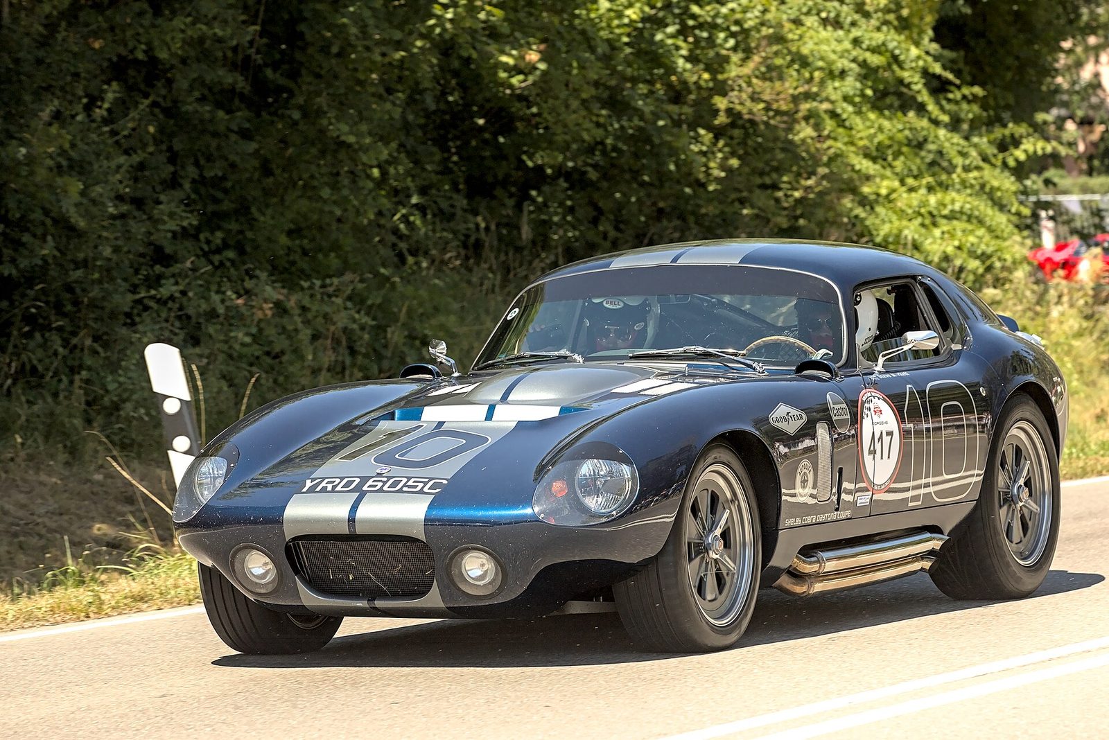 A dark blue Shelby Cobra Daytona Coupe with white stripes on a country road