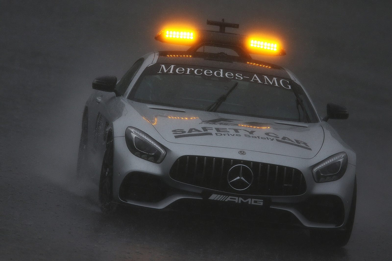 A Mercedes-AMG GT S safety car with its lights on in heavy rain
