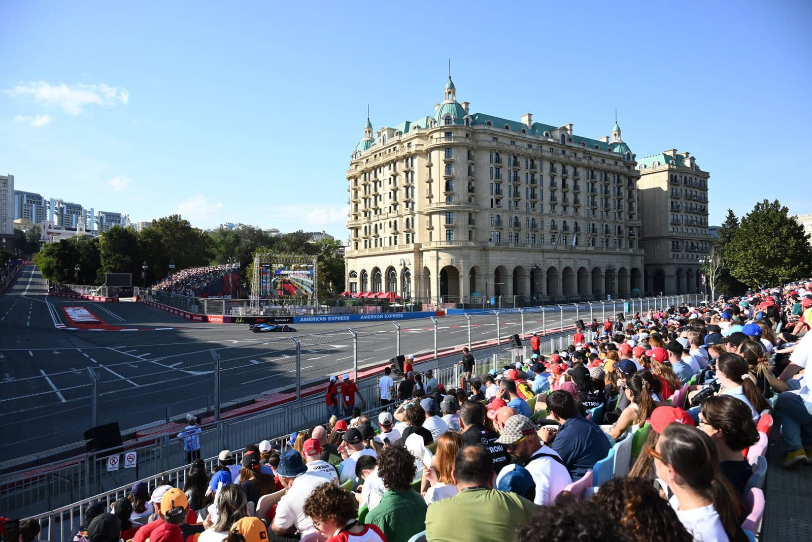A Formula 1 car in a slow corner in front of a large hotel and a full grandstand at the 2026 Azerbaijan Grand Prix in Baku