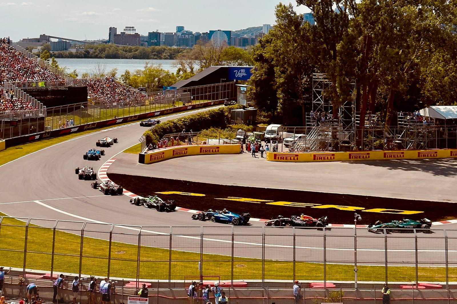 Formula 1 cars in single file through the first two corners on the opening lap of the 2025 Canadian Grand Prix, with the river and the city behind