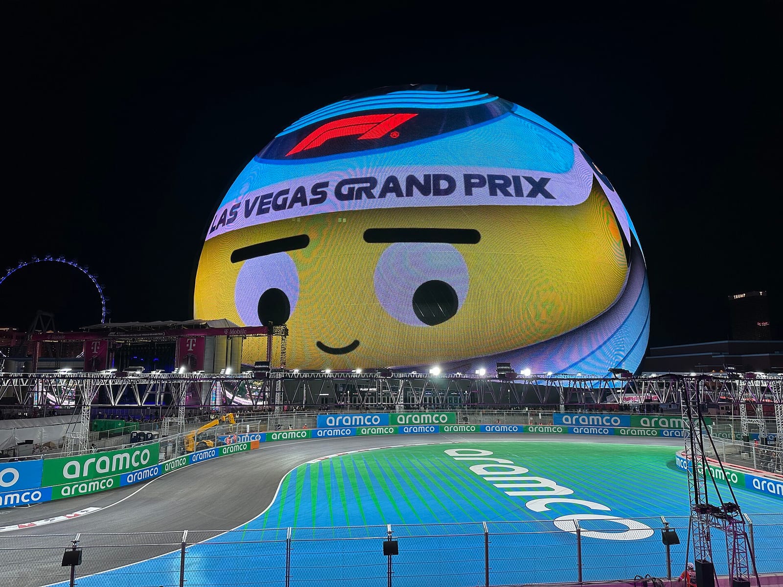 The Sphere lit up with a yellow face and a Las Vegas Grand Prix banner at night, with the track and its painted run-off area in the foreground