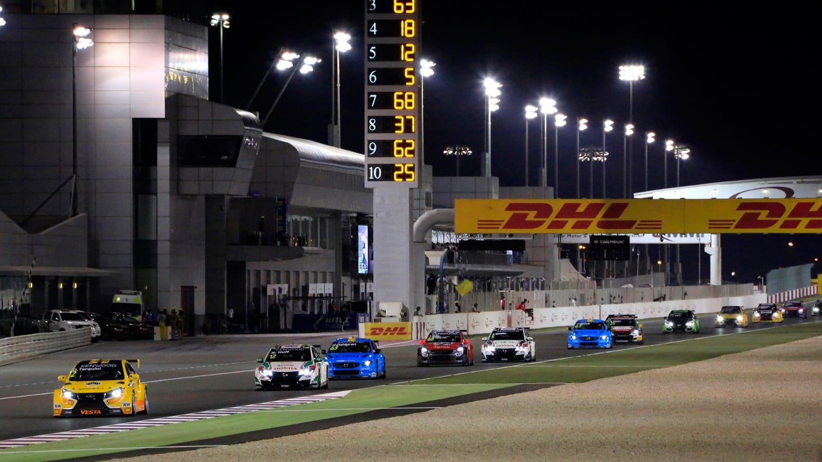Touring cars on the pit straight of the Lusail circuit at night in 2016, with the pit building and the timing tower behind them