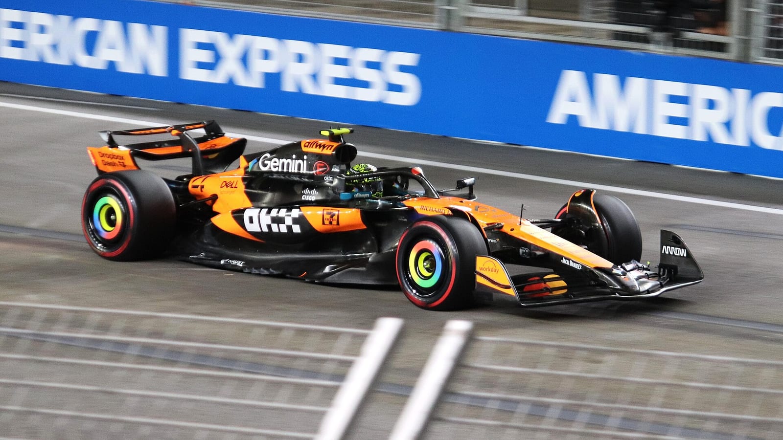 Lando Norris's orange McLaren MCL39 passing a blue advertising board in Singapore during second practice in 2025