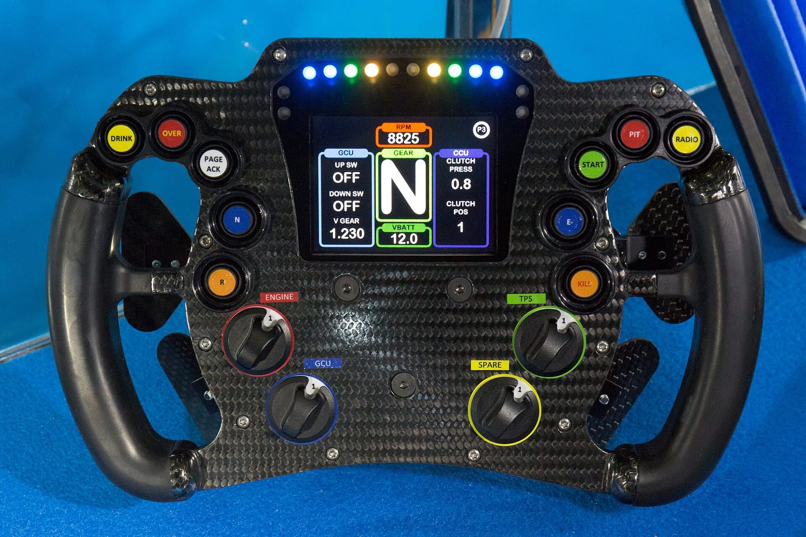 Carbon racing steering wheel with a colour display in the middle, shift lights on top and rotary switches below