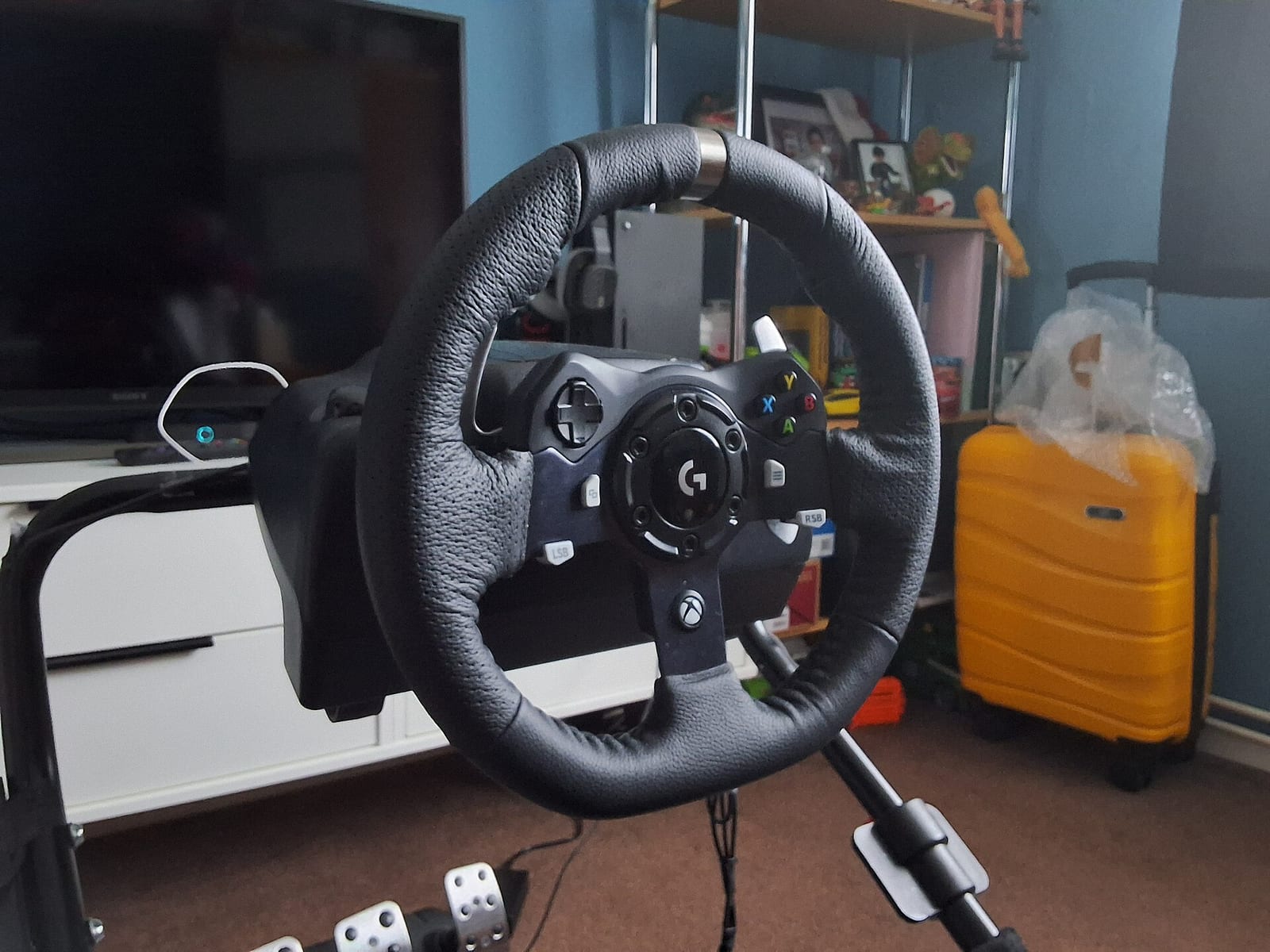 Logitech G920 steering wheel with Xbox buttons mounted on a wheel stand in front of a TV