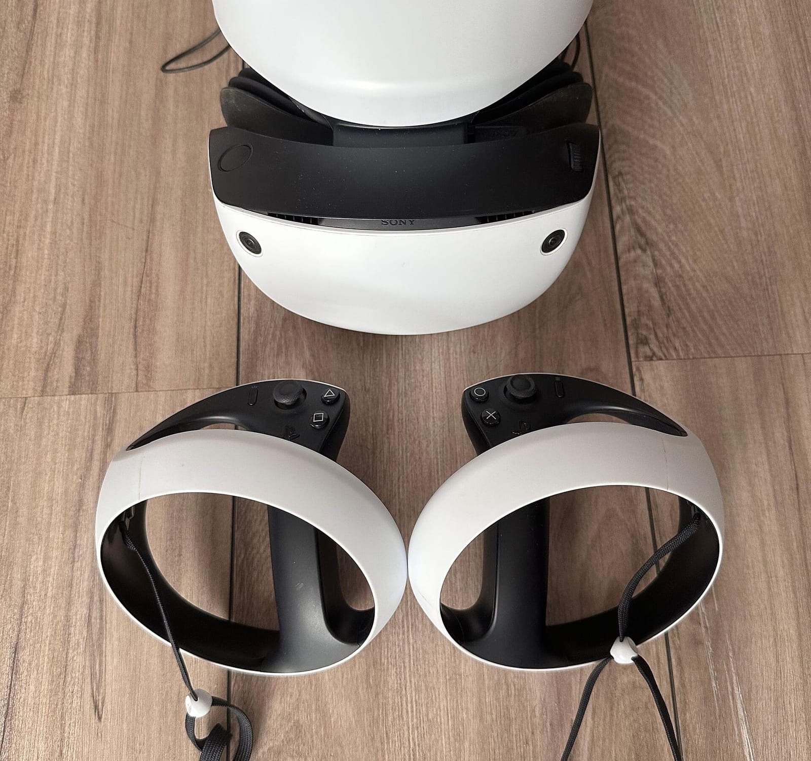 PlayStation VR2 headset and its two Sense controllers on a wooden floor