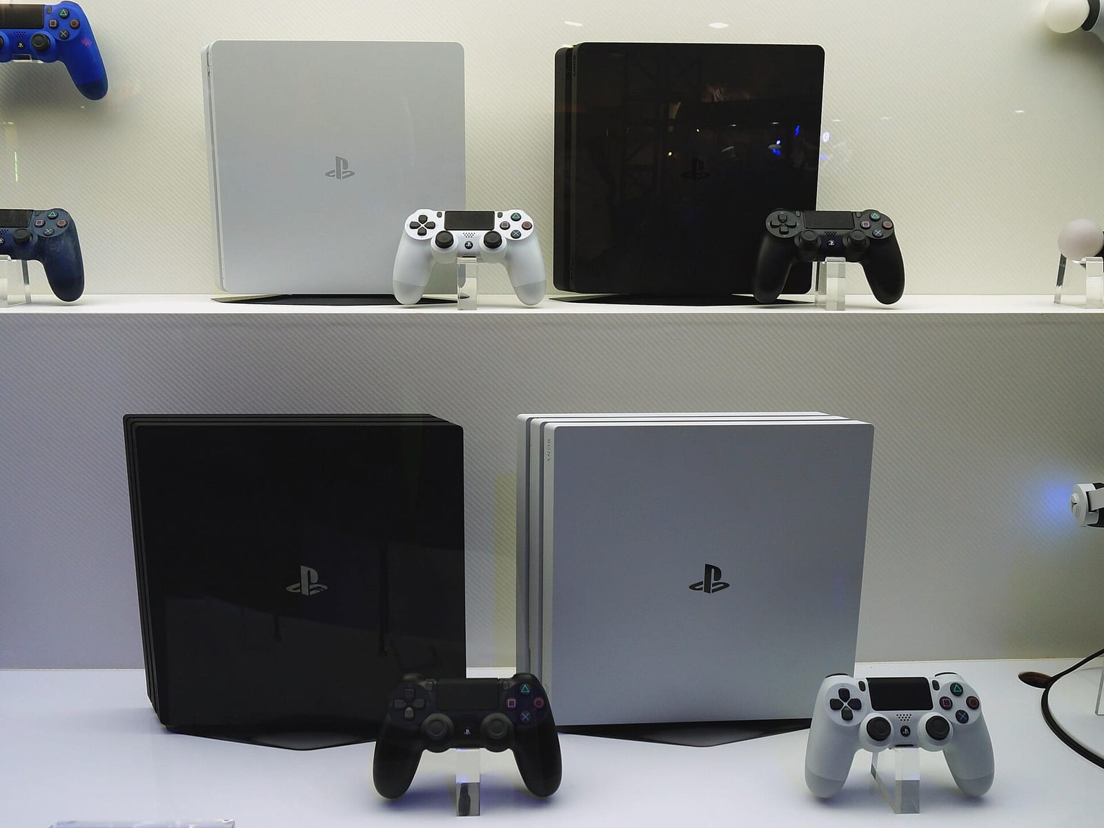 White and black PS4 Slim and PS4 Pro consoles with DualShock 4 controllers on a shop display