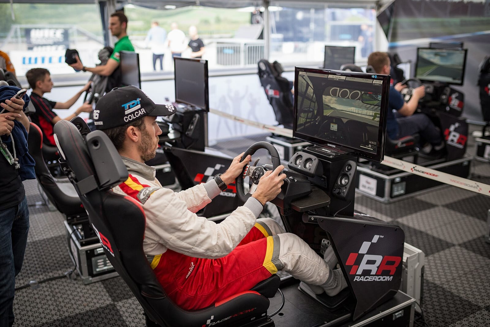 A racing driver in a sim racing cockpit with a wheel and a single screen at a touring car paddock