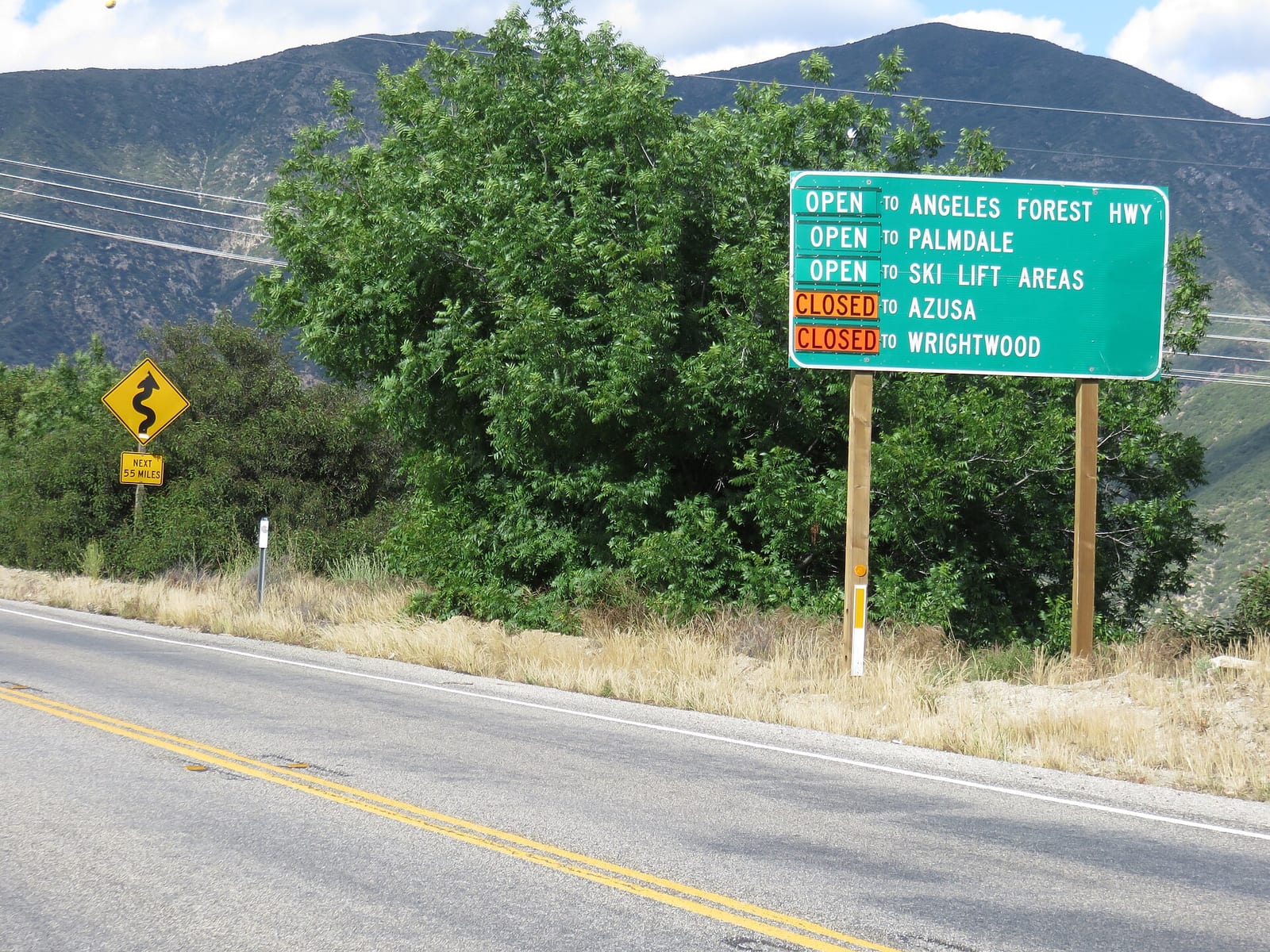 Road sign at the entrance of the Angeles Crest Highway showing which sections are open, with the mountains behind
