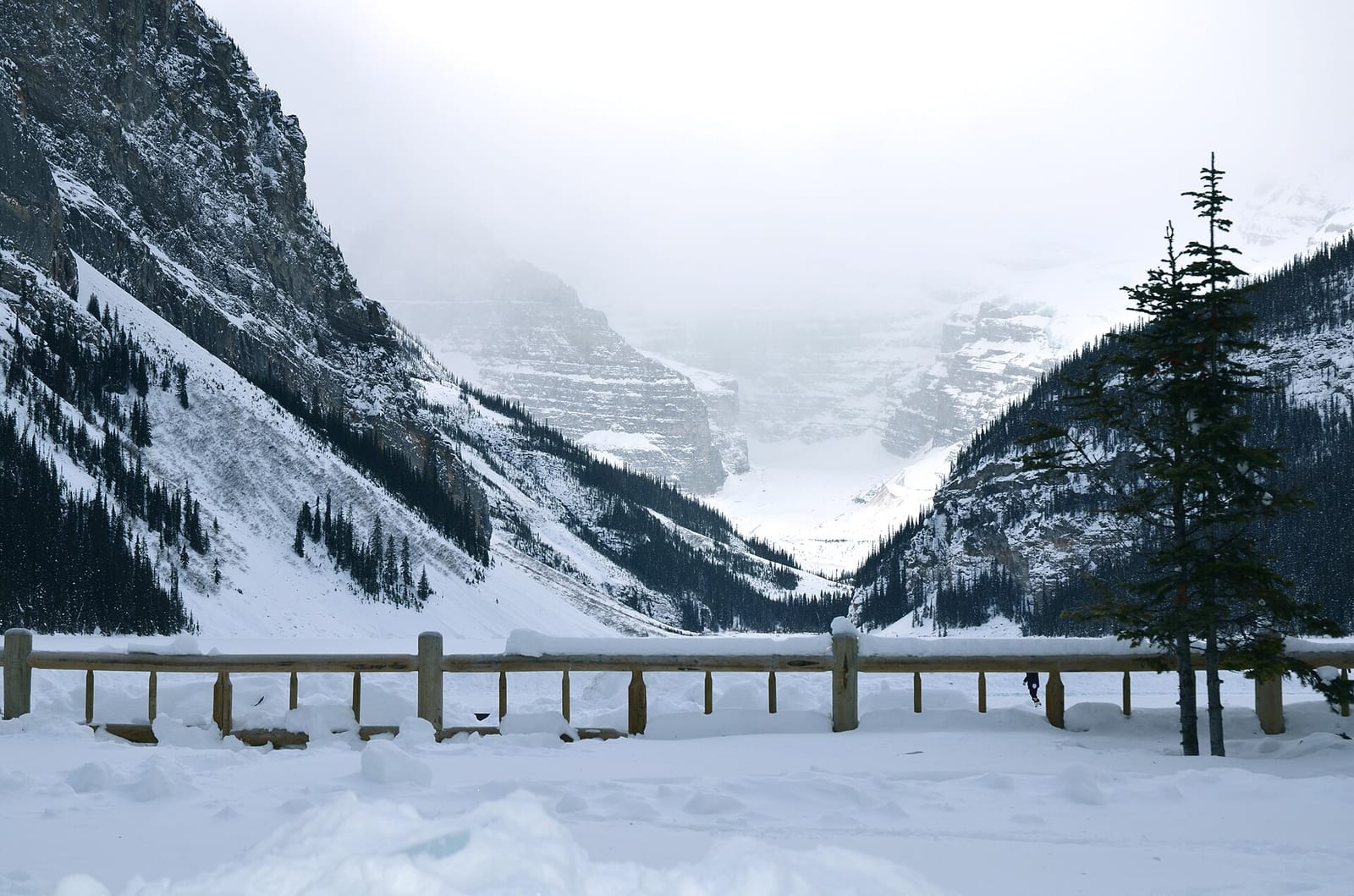 Frozen Lake Louise in winter with snow covered mountains and a wooden fence in the foreground