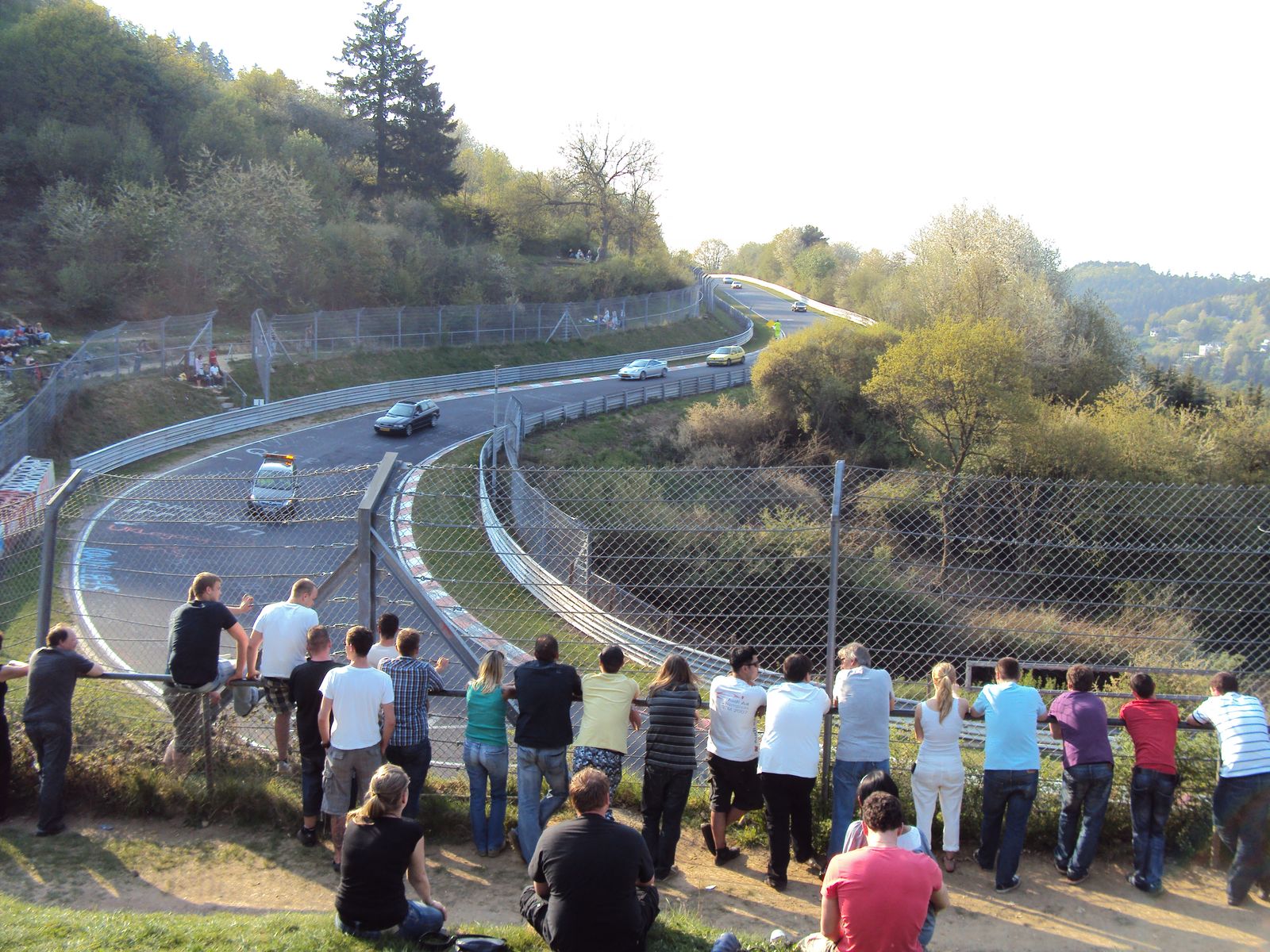 Road cars on the Nordschleife at Wehrseifen with spectators along the fence on a spring evening