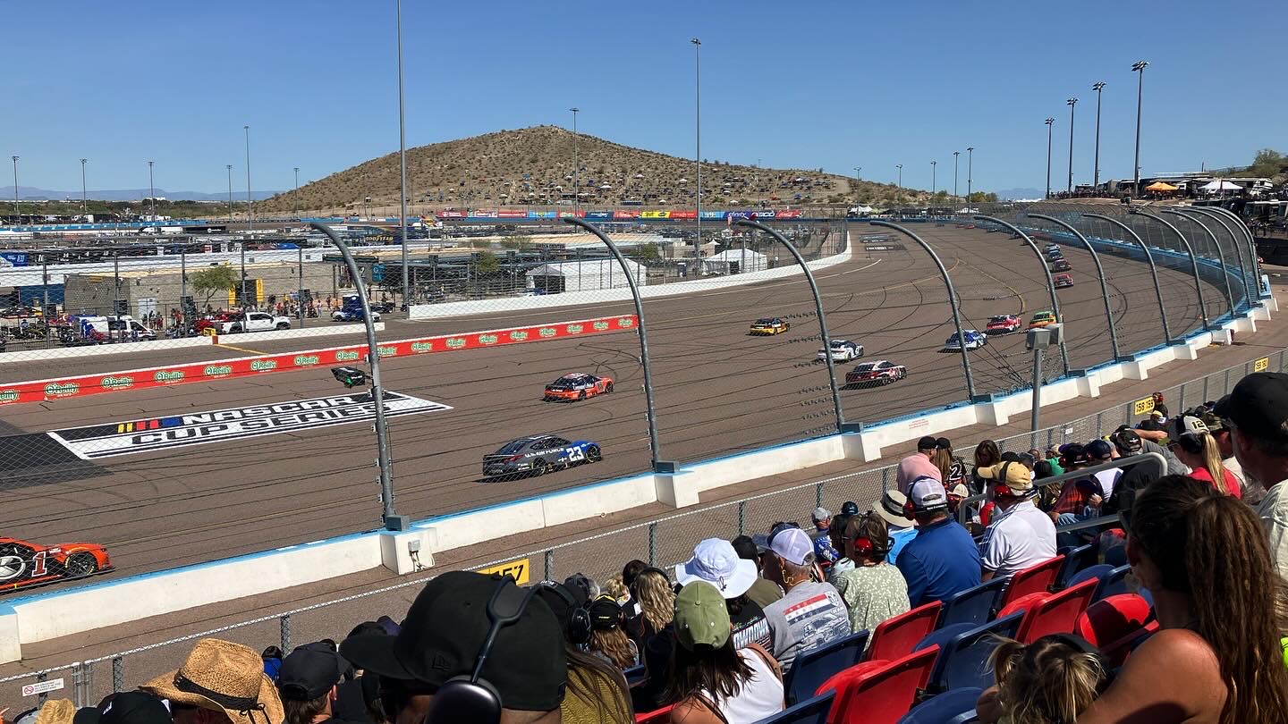 Cup cars running single file through the turns at Phoenix Raceway in front of the grandstand in 2024
