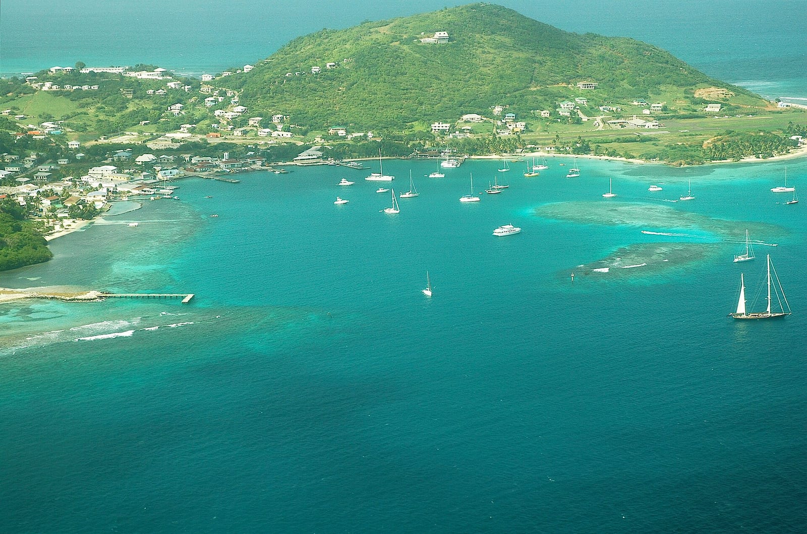 Aerial view of Clifton on Union Island with sailing boats in the turquoise bay and green hills behind